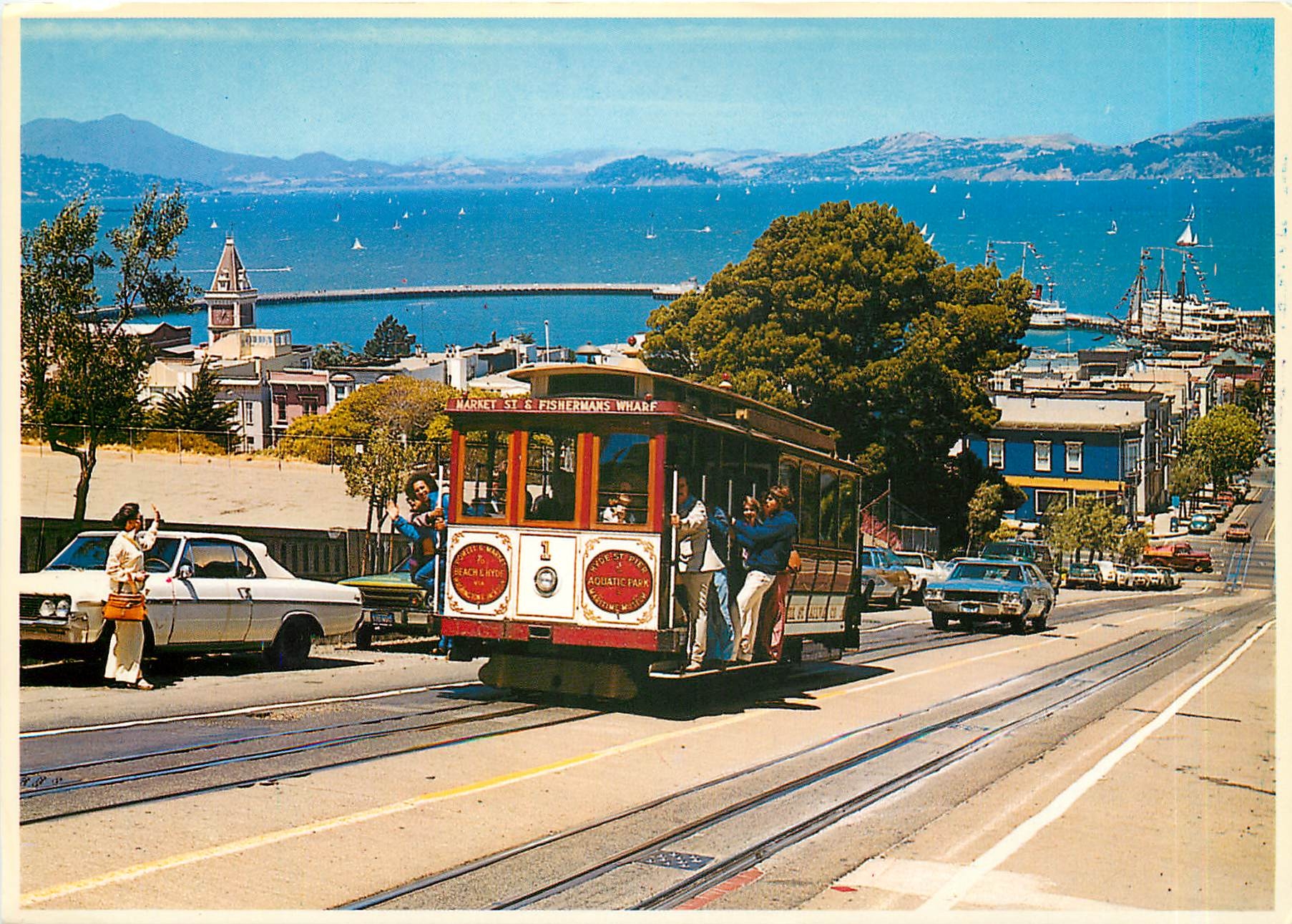 CPM Cable Car climbs a steep San Francisco hill as sailboats navigate the bay 