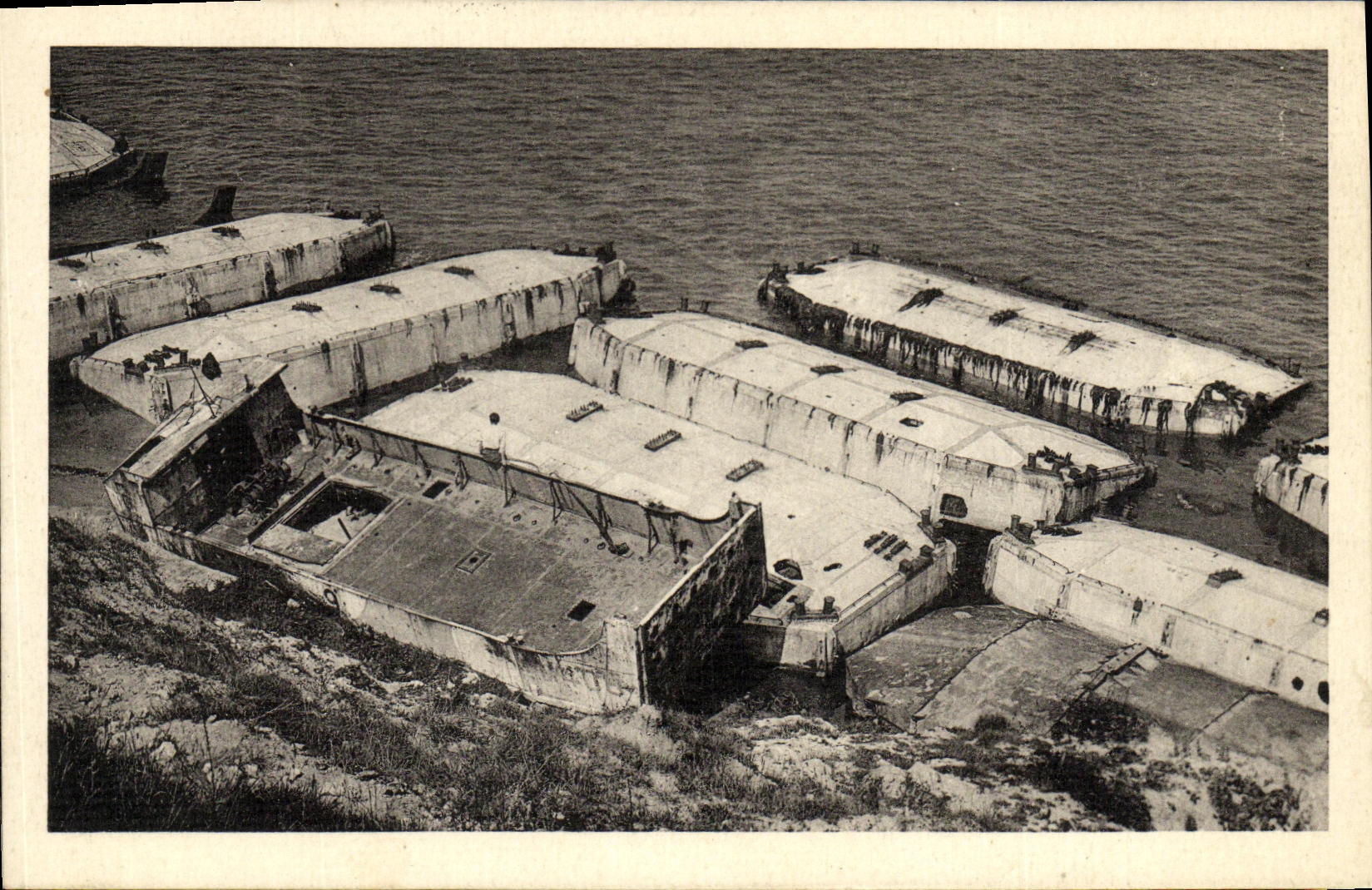 Los barcos de Arromanches Petits de la POSTAL de la VENDIMIA flotan del uso del cemento para la descarga de Militaria