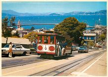 CPM Cable Car climbs a steep San Francisco hill as sailboats navigate the bay 