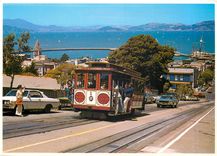 CPM Cable car climbs a steep San Francisco hill as sailboats navigate the bay 