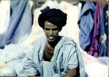 CPM L'Afrique En Couleurs Naturelles Marchand Maure au milieu De Ses Tissus